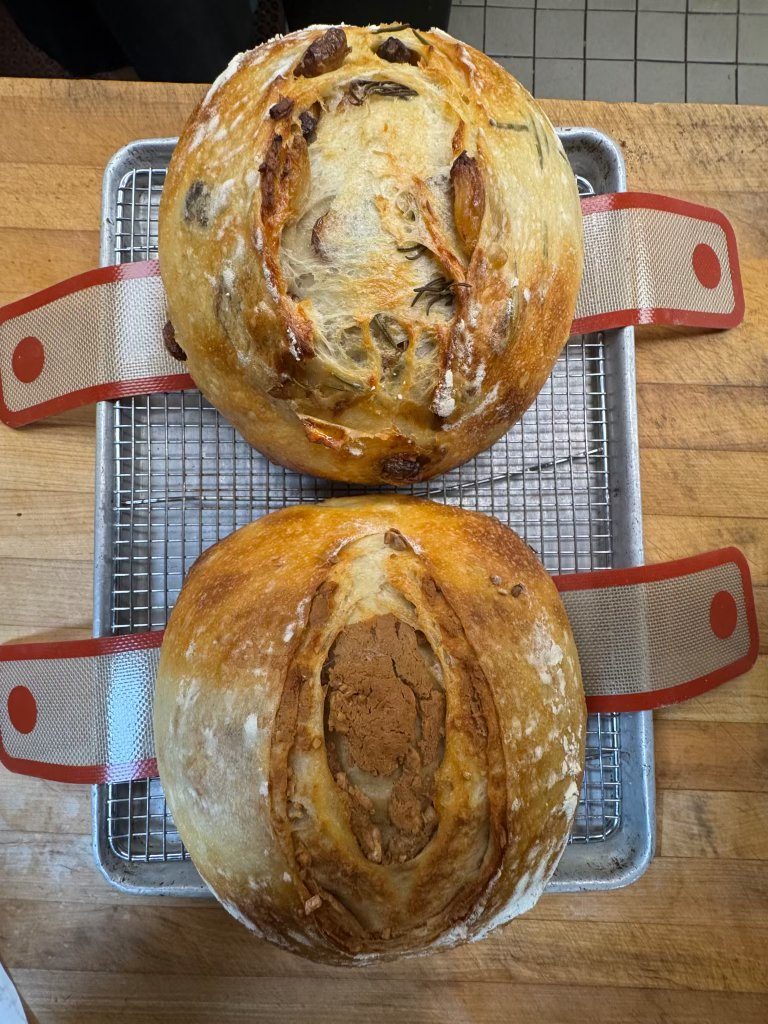 Two scored sourdough loaves cooling on a rack