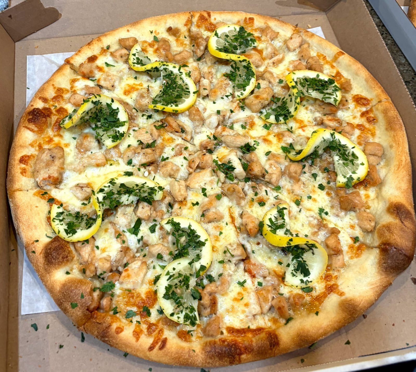 Pizza topped with chicken, lemon slices and parsley